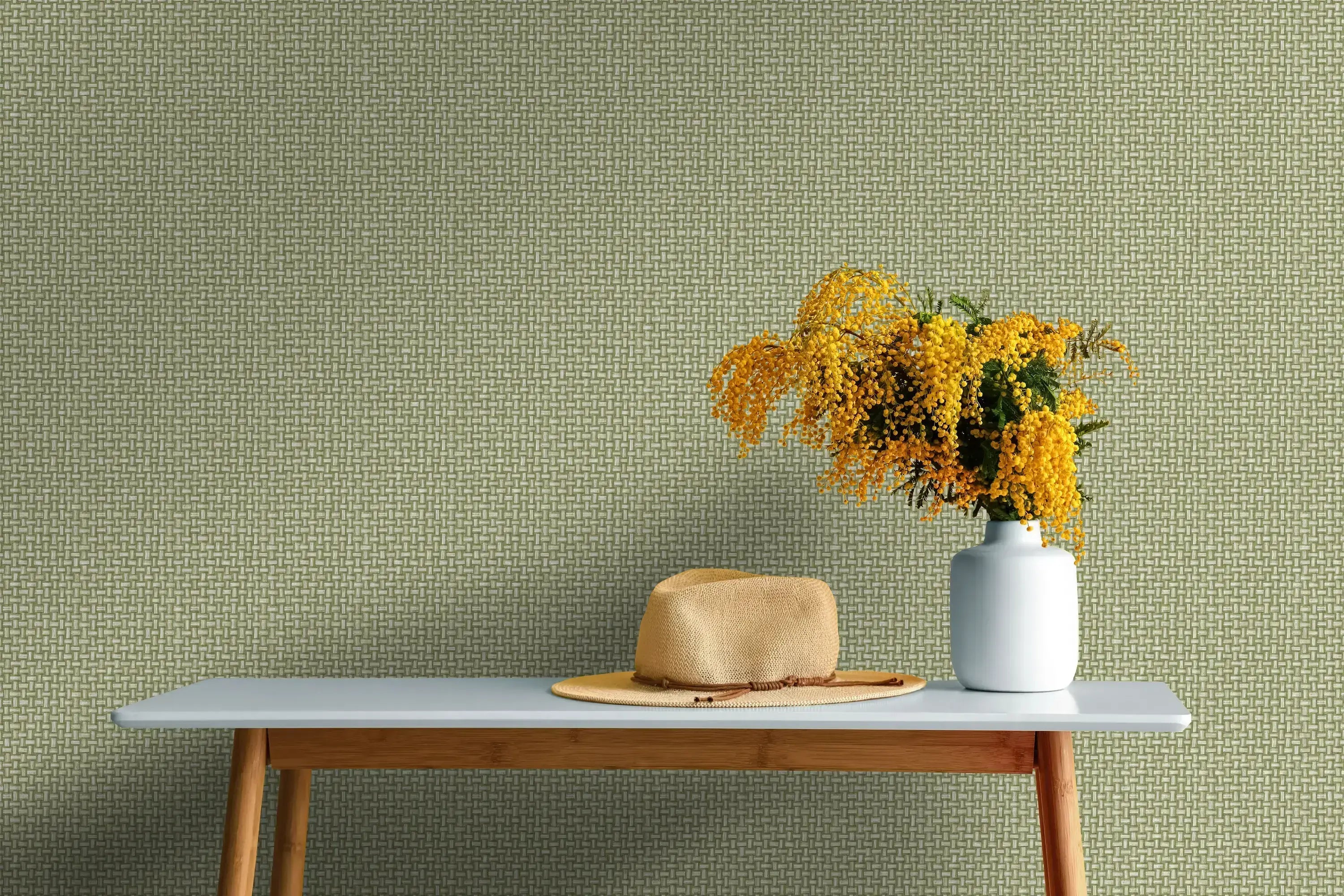 Interiørscene med Biderbost Weave - Green tapet på væggen, bord med hat og vase med gule blomster.