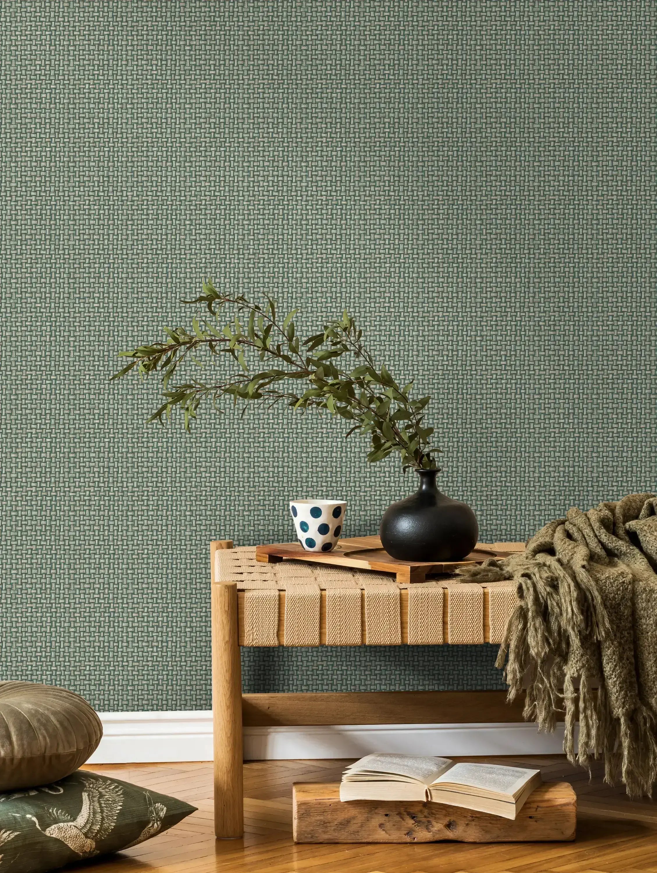 Interiør med en væg dekoreret med Biderbost Weave - Teal tapet. En bænk med en pude og en vase med grene står op ad væggen.