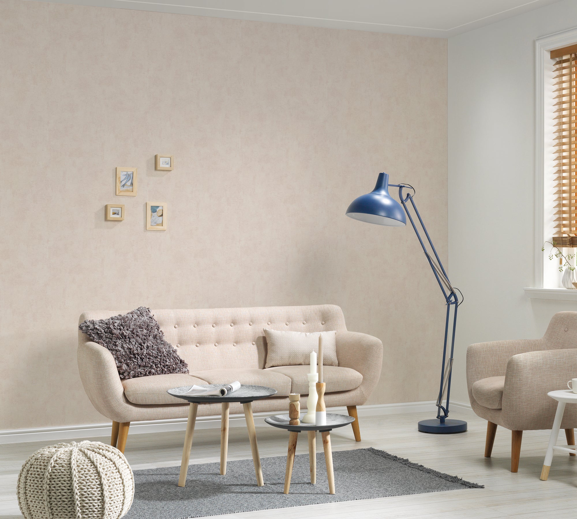 Indretning af stue med Clouded Brushstroke - Sand tapet på væggen. Moderne møbler, herunder en beige sofa, blå lampe og kaffeborde, komplementerer tapetets bløde sandfarve.