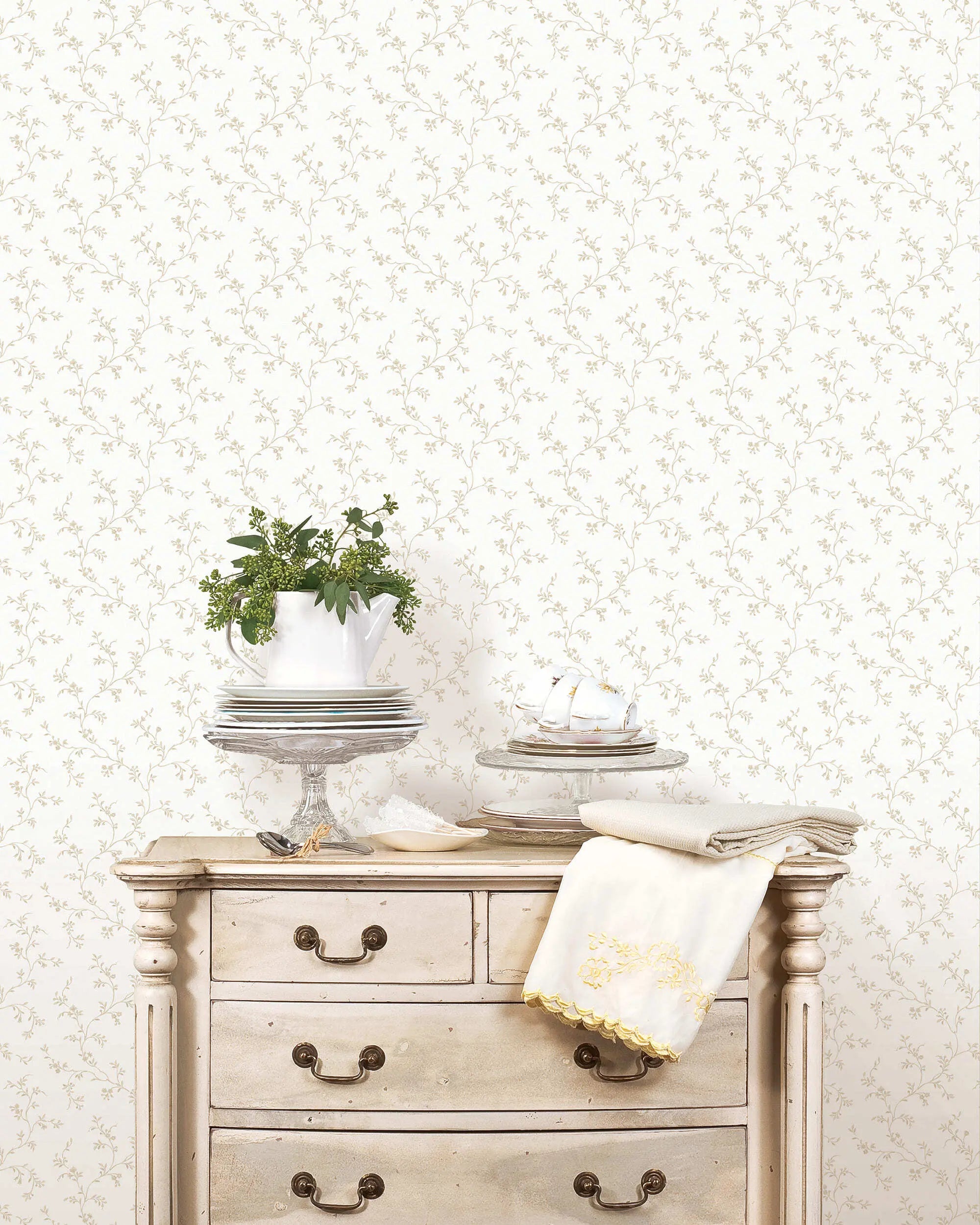 Wallpaper Floral Silhouette - Ivory Breeze fra Nicetapet.dk i et interiørmiljø med en antik kommode og borddækning foran det subtile blomstrede tapet.