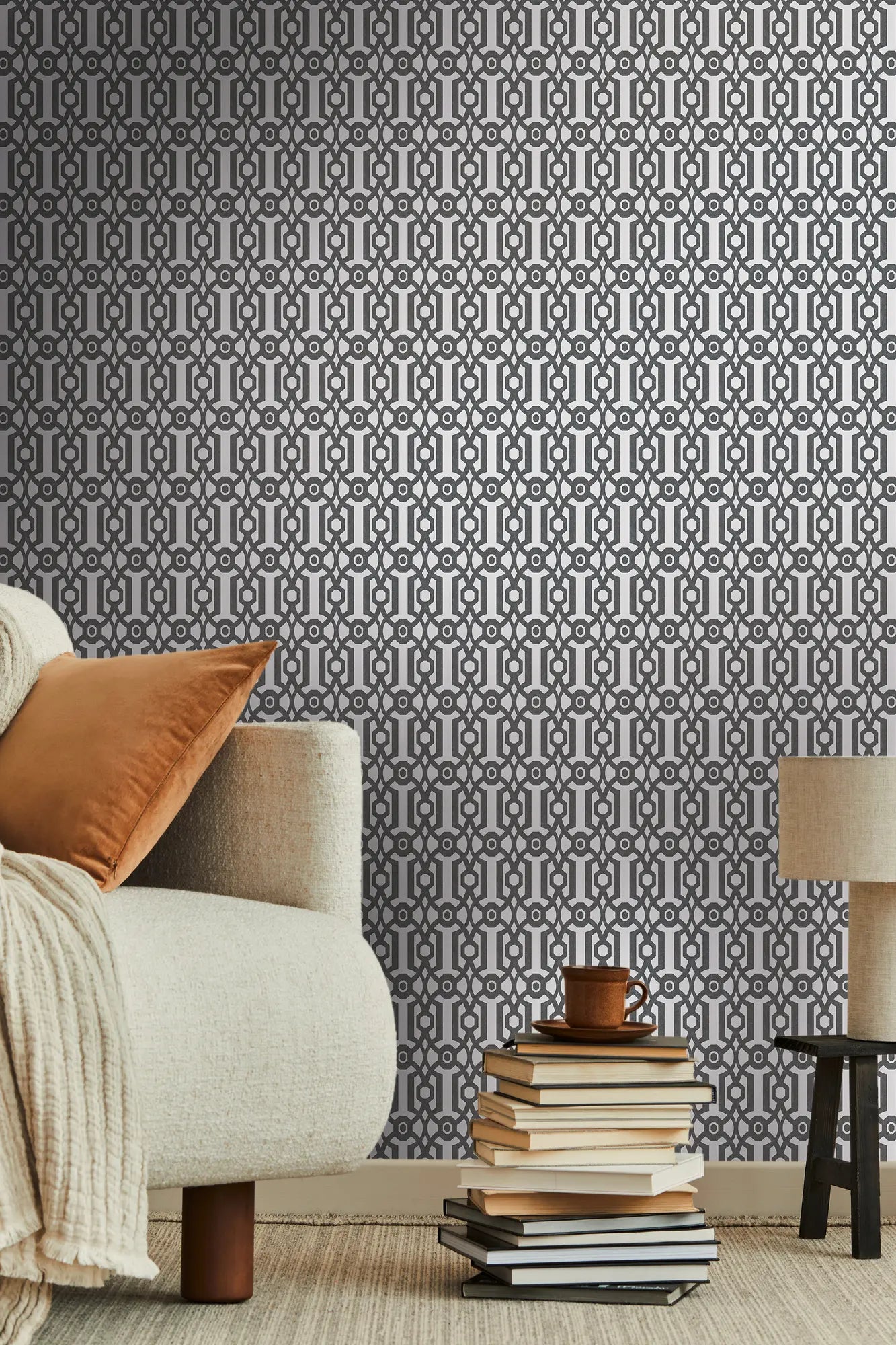 Tapetet Lattice Delight - Charcoal Elegance monteret på en væg, der viser en stilfuld indretning med en sofa, puder og stablede bøger.