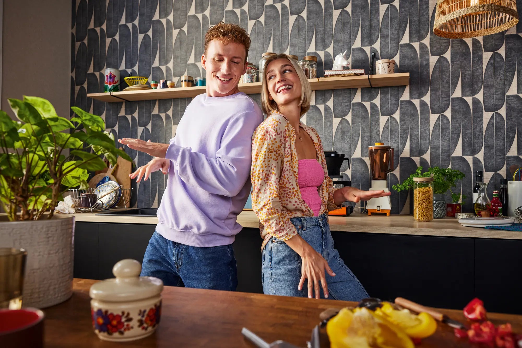 Køkken med Leafy Leaves - Slate tapet på væggen og to personer i baggrunden, der smiler.