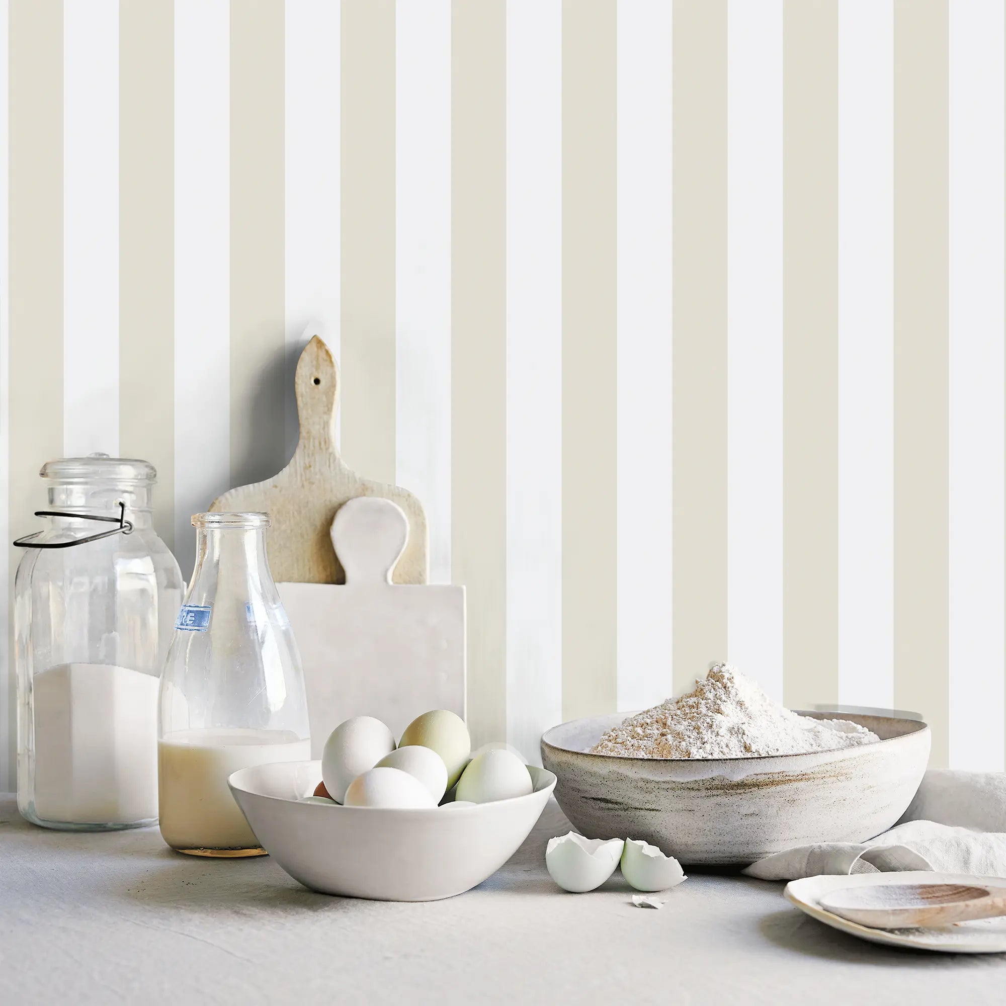 Morning Stripes - Linen tapet i et køkkenmiljø med beige og hvide striber, som komplimenterer køkkenelementer som æg, mel og en flaske mælk.