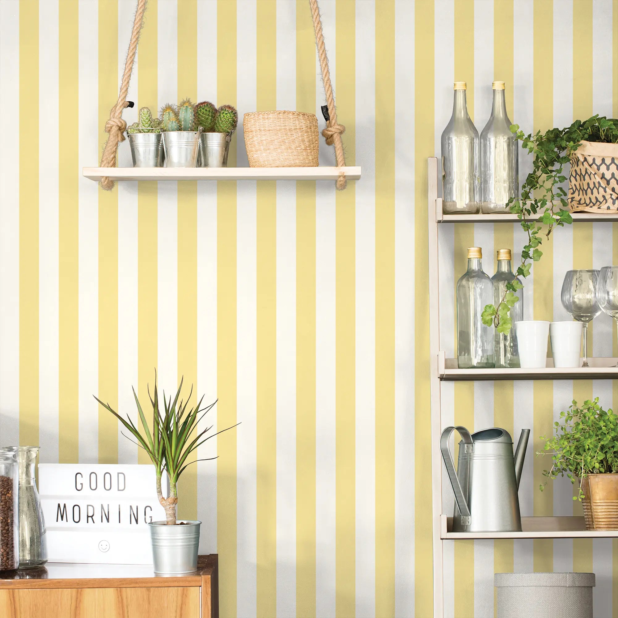 Tapet 'Morning Stripes - Sunshine' med gule striber, indrettet med hylder, planter og dekorative elementer i et hjem.