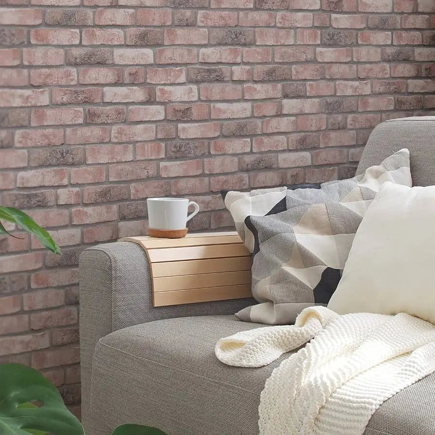 Stue med Rosy Bricks - Sandstone tapet, beige sofa, puder og en hvid kop på armlænet.