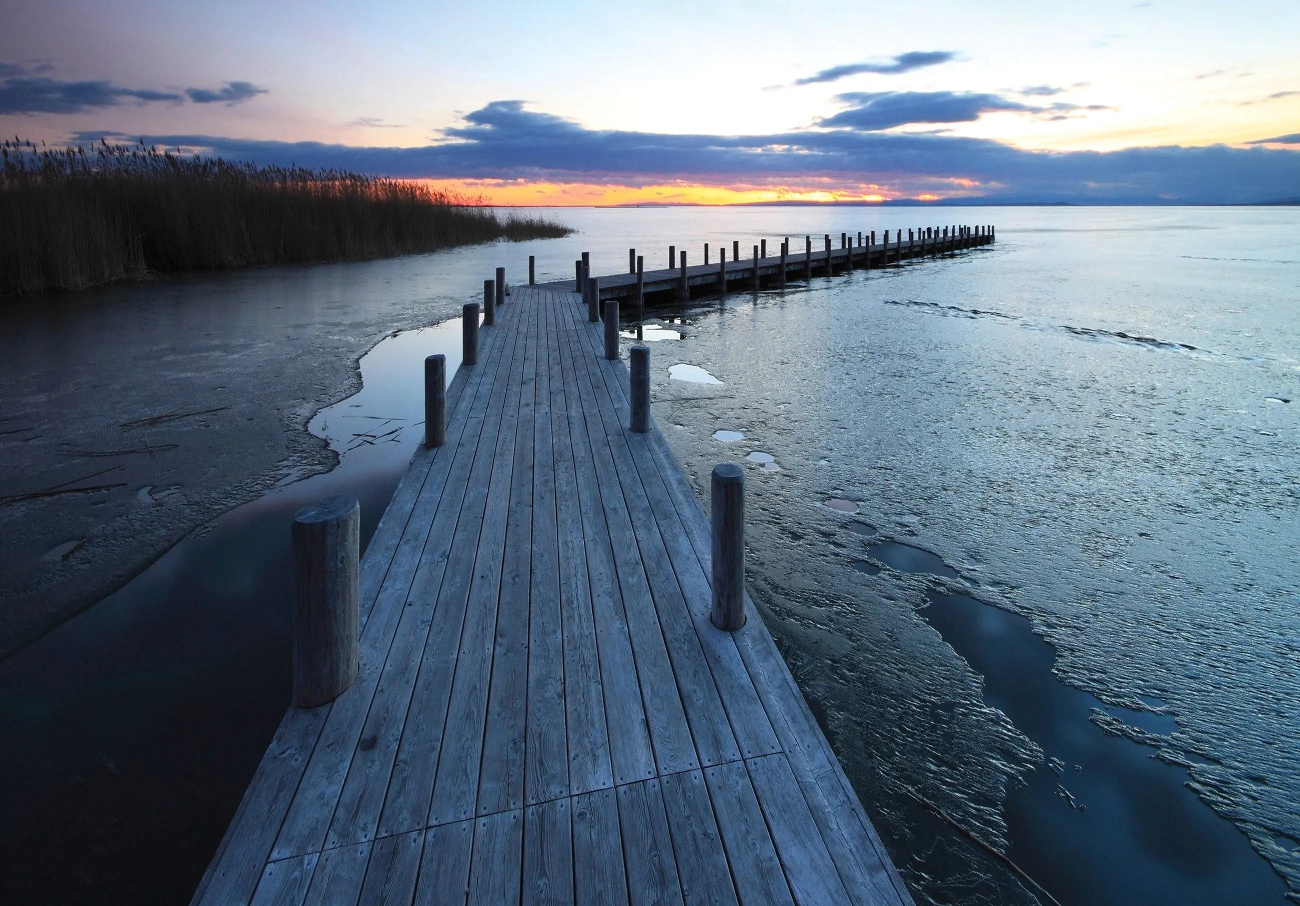 Billede 7 af Fototapet - Træbrygge ved solnedgang med delvist isdækket vand