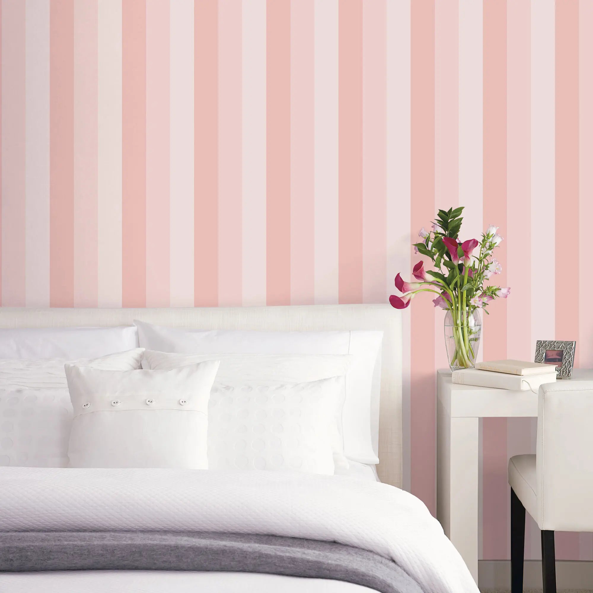 Veiled Stripes - Blush tapet dekorerer en soveværelsesvæg med en seng, hvide puder og et skrivebord med blomsteropstilling.