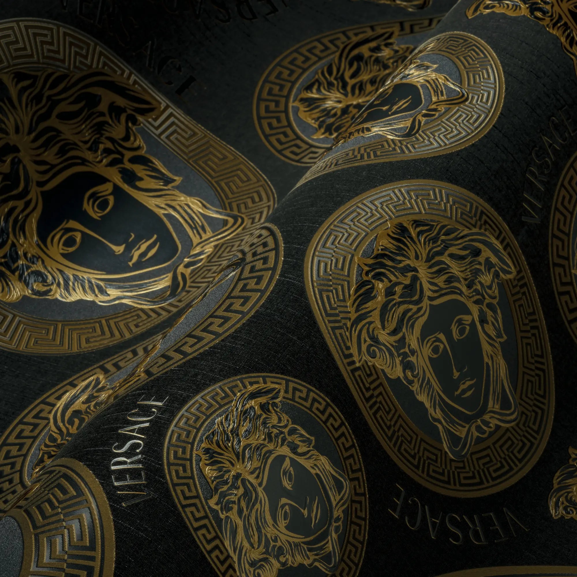 Detaljeoptagelse af Versace Medusa Amplified tapet i kul, der viser de gyldne Medusa-mønstre og tekstur.