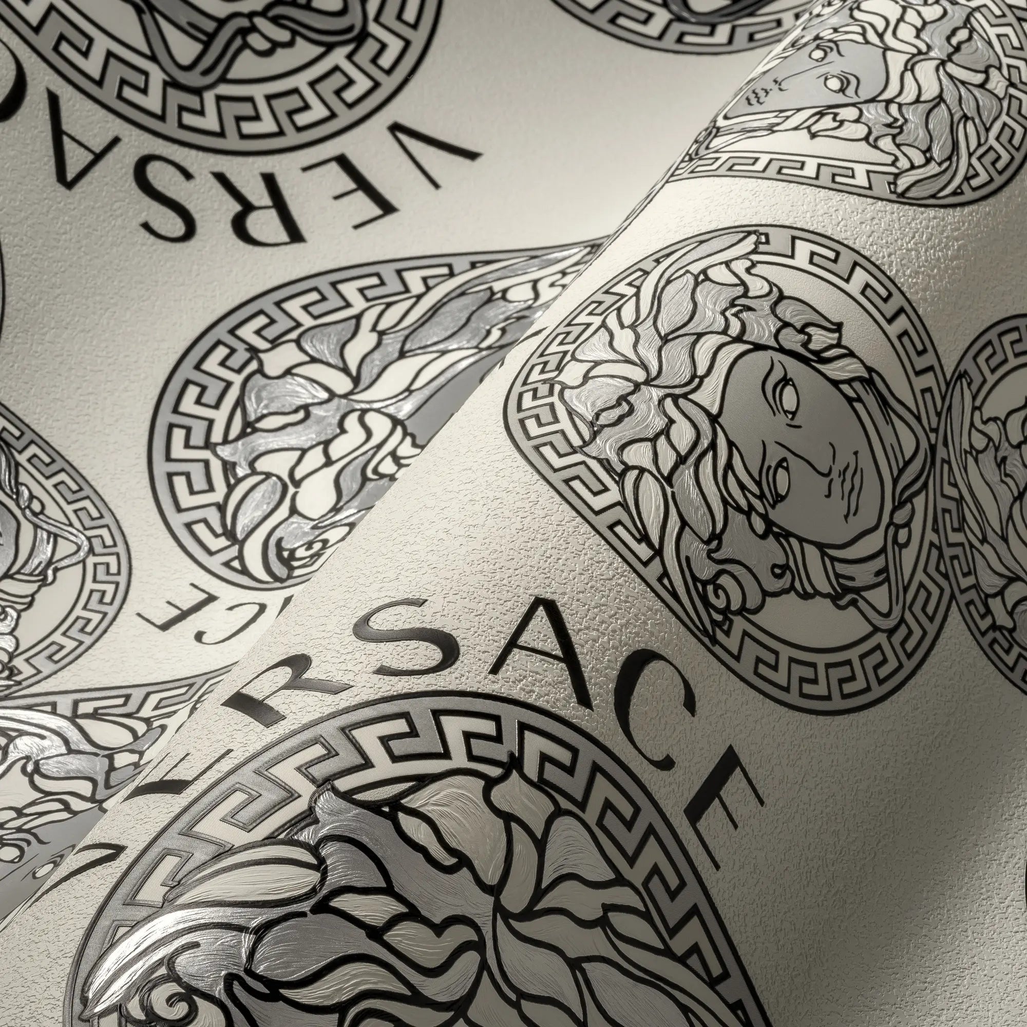 Nærbillede af tapet med et Medusa-motiv og Versace-tekst i sølvgrå toner. Produktnavn: Versace Medusa Amplified - Silver Gray.